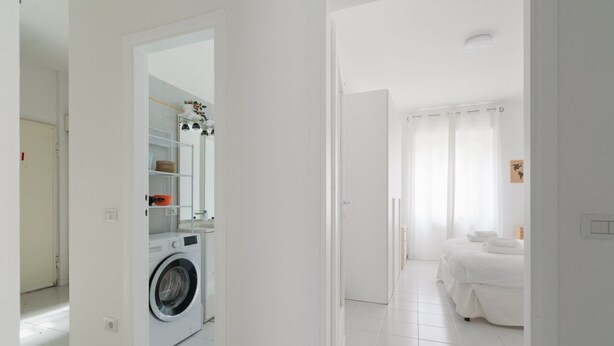 Een moderne hotelkamer met een wasmachine, een bed en een badkamer met een spiegel en planken.