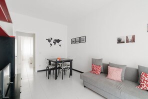 A modern living room with a grey sofa, a dining table with chairs, a flat-screen TV, and a world map on the wall. - GuestHost - Comfy Apartment M2 Udine (Milan)