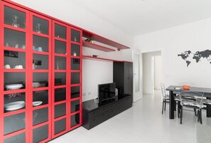 A modern kitchen with a red cabinet, black countertop, and a dining area with a black table and chairs. - GuestHost - Comfy Apartment M2 Udine (Milan)