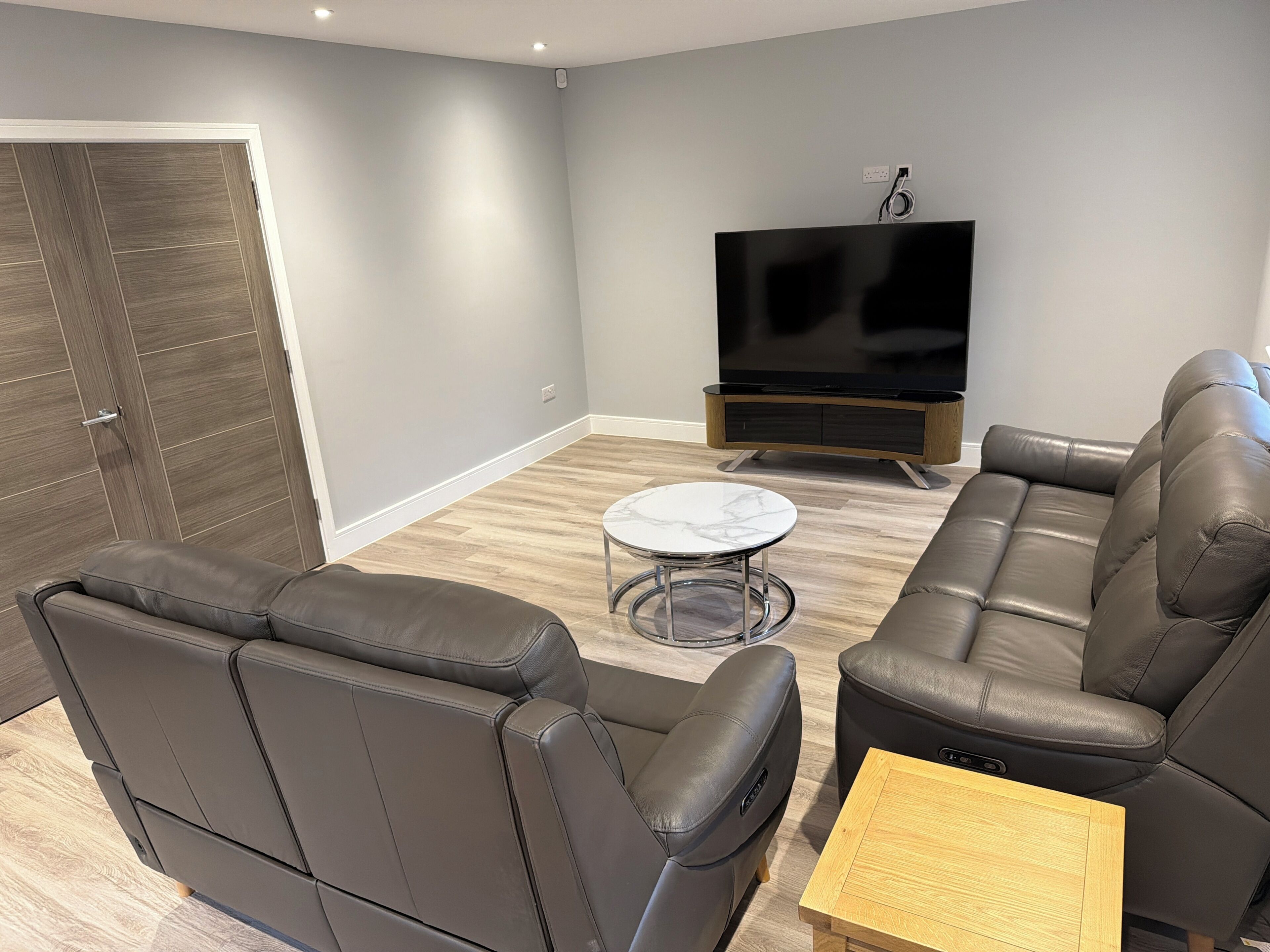A modern living room with a sectional sofa, a small round table, and a flat-screen TV.