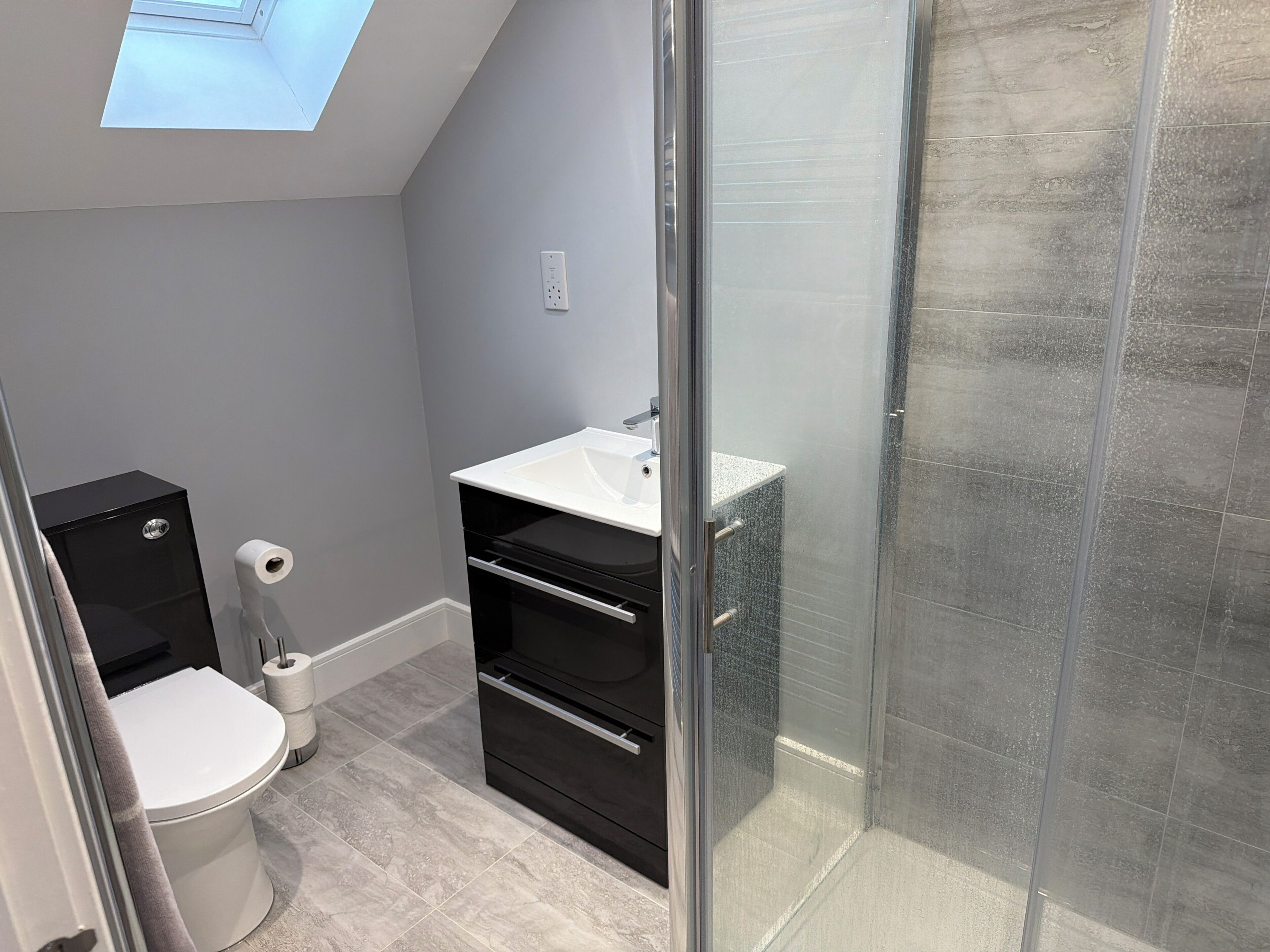 Une salle de bain moderne avec un puits de lumière, des toilettes, un lavabo et une douche.