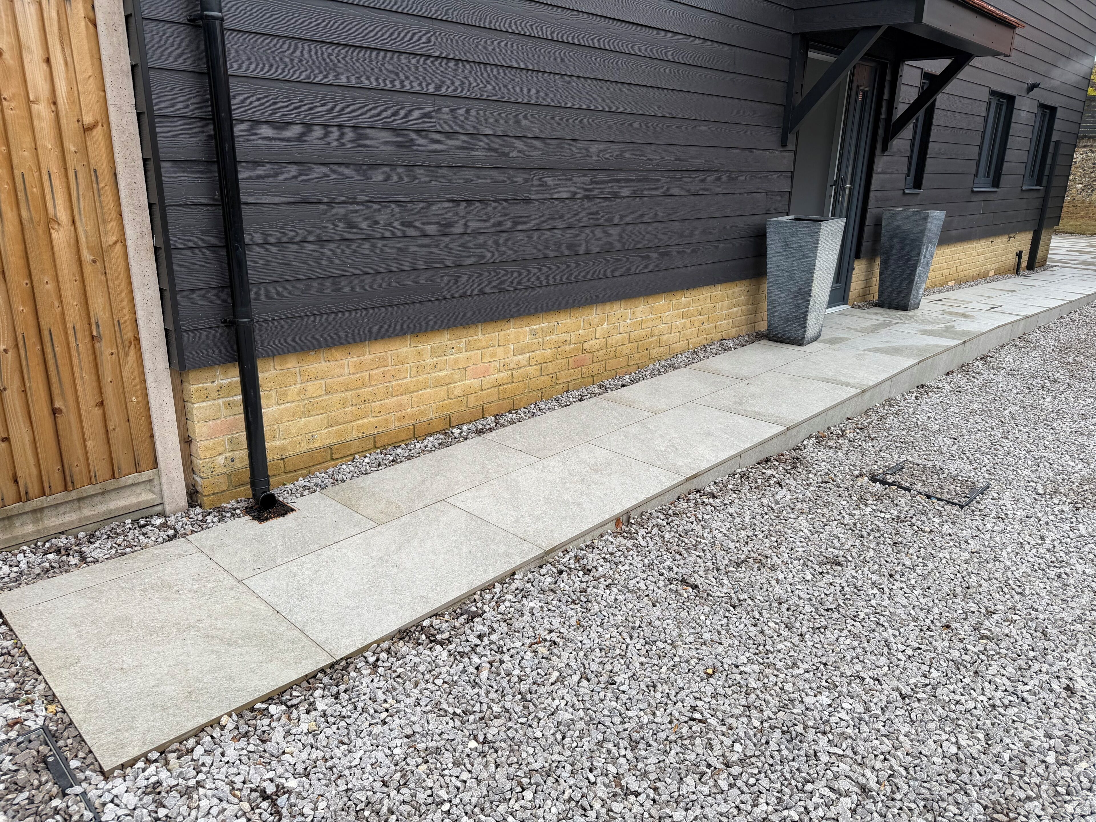A building exterior with a dark siding, a brick base, and a concrete pathway.