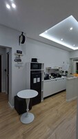 Una cocina moderna con armarios blancos, un refrigerador negro, un microondas y una cafetera. En el centro hay una mesa redonda blanca.
