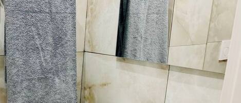 Un baño con un lavamanos blanco, un espejo y dos toalleros con toallas grises.