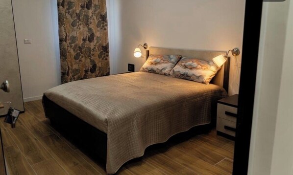 A bedroom with a bed, nightstands, a lamp, and a curtain.