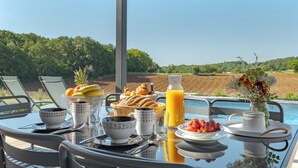 A breakfast table with breakfast items, a vase of flowers, and a view of the landscape. - Les Huttes (Montgesty)