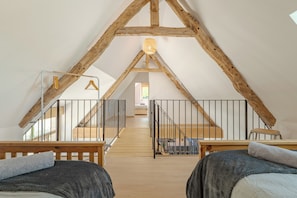Quarto no estilo loft com vigas de madeira aparentes, escada de madeira e vista para o quarto vizinho.