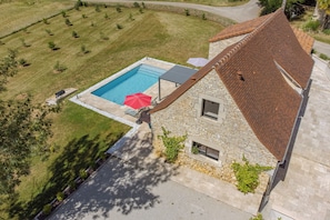 Une maison en pierre avec une piscine, un patio doté d’un parasol et un chemin en pierre.