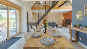 A dining area with a wooden table set for six, a staircase, and a view of the outdoors. - Les Huttes (Montgesty)