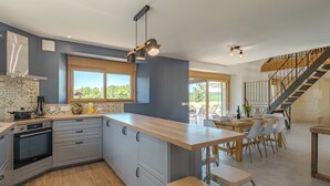 A modern kitchen with a central island, built-in oven, and a dining area with a wooden table and chairs. - Les Huttes (Montgesty)