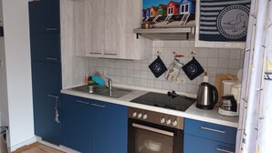 A kitchen with blue cabinets, a stainless steel sink, a stove, and a microwave. There are decorative wall hangings and a painting above the sink.