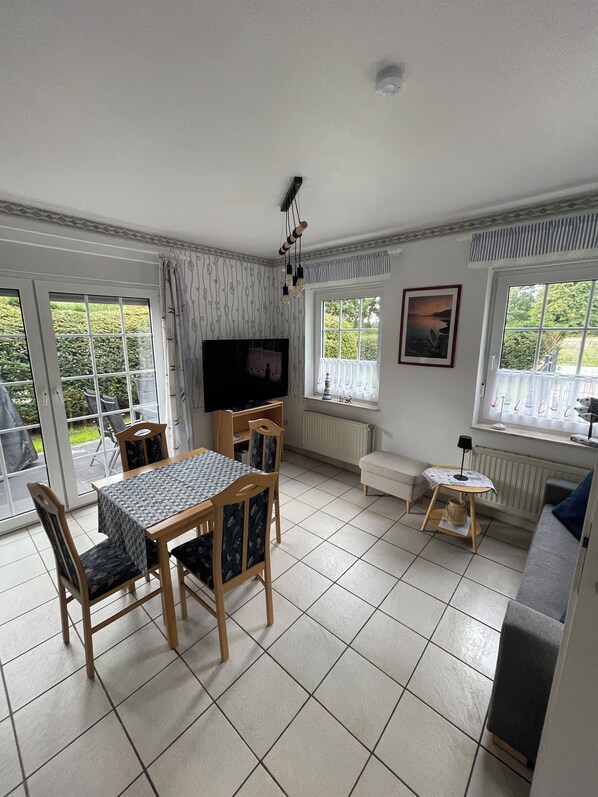 A dining area with a table and chairs, a television, and a window with curtains. - The Aurich-Tannenhausen Vacation Home right on the shore of the swimming lake! Pets welcome! (Aurich)