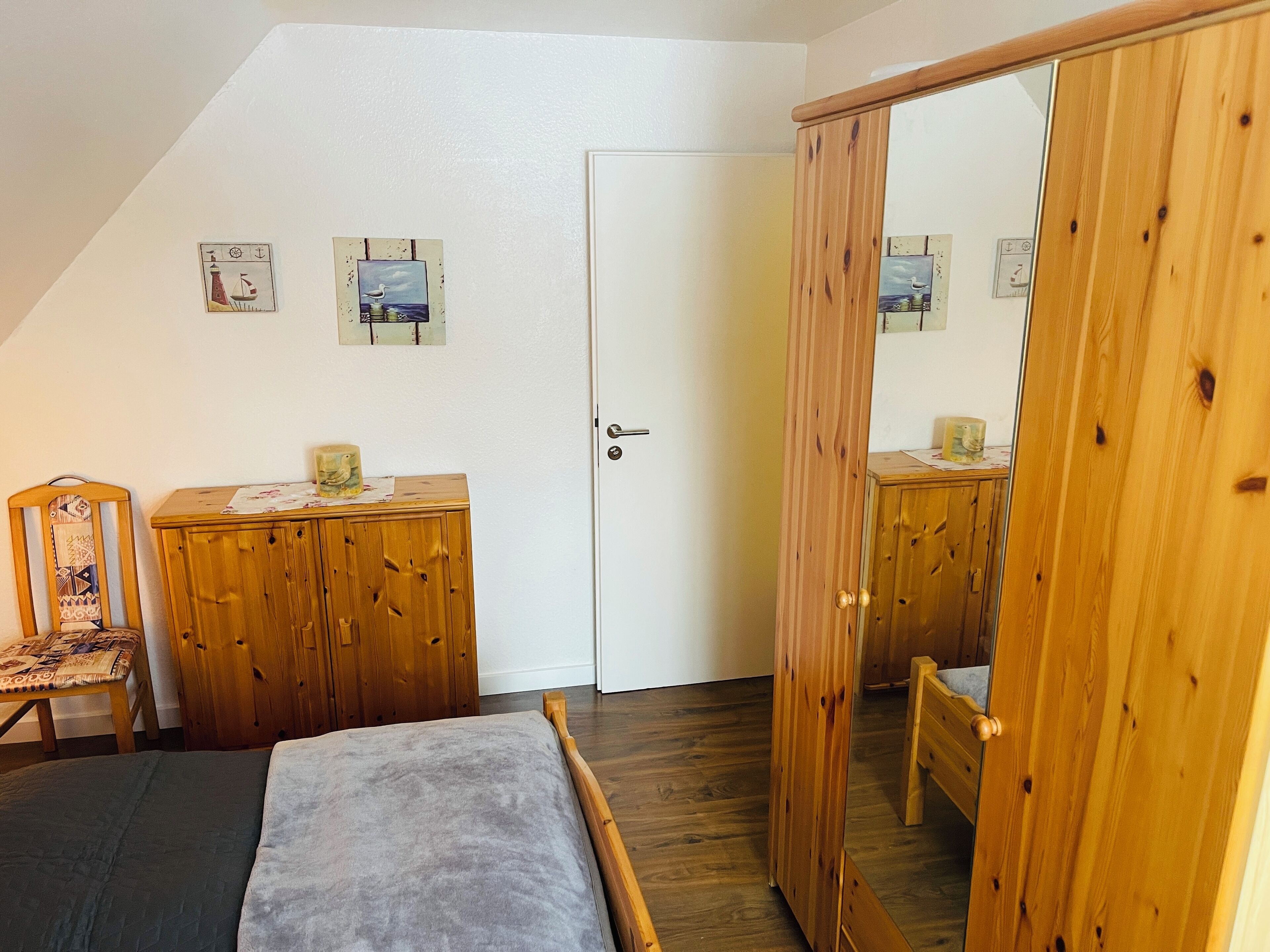 Une chambre avec un plafond en pente, des meubles en bois, un lit, une chaise, une armoire et une porte.