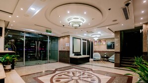 Un'ampia hall d'albergo con un grande design circolare a pavimento, una reception, un'area salotto e una scala che conduce ai piani superiori.