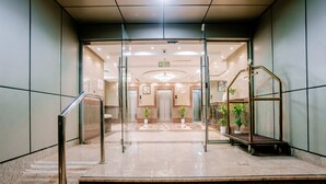 Una hall d'albergo con pavimento in marmo, ingresso in vetro e ascensore in metallo.