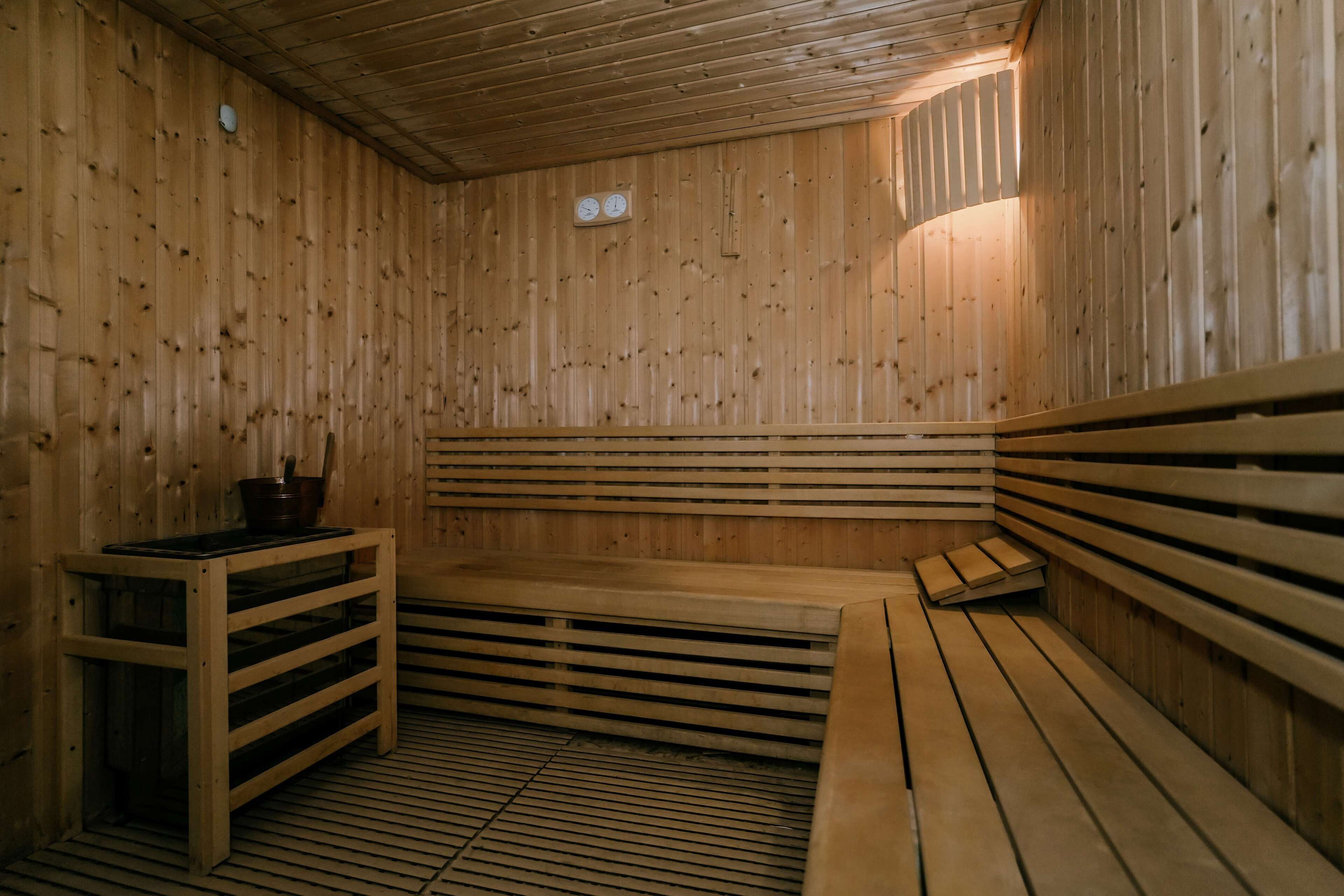 A sauna with wooden benches and a table, a clock on the wall, and a sloped ceiling.