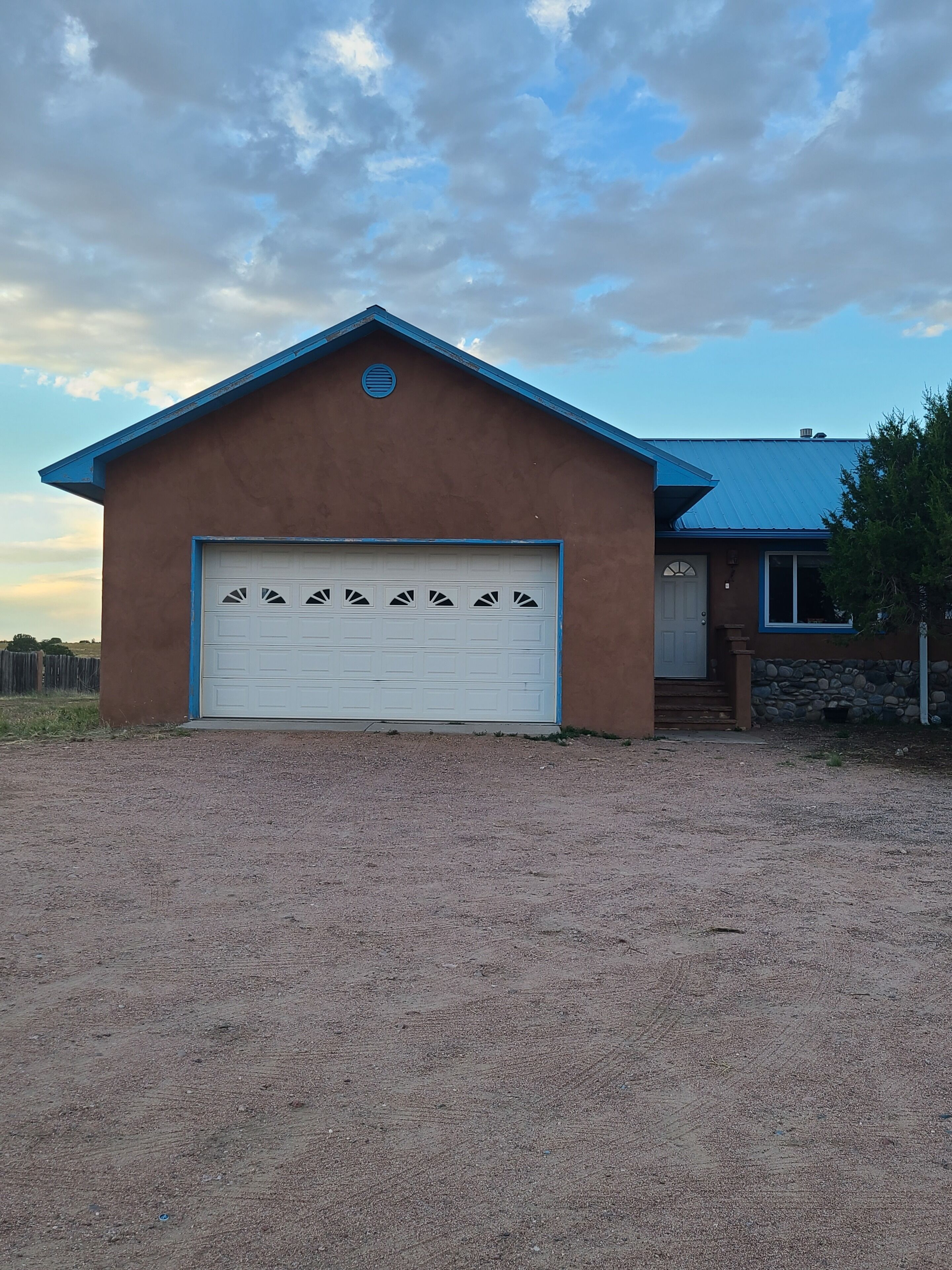 A single-story house with a brown exterior and a blue roof. It features a white garage door with decorative cutouts.