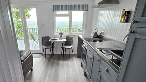 A modern kitchen with a dining area, large windows, and a view of the countryside. - 1 Bed Cabin-sleeps 2, Hot Tub, Garden, Views, Pets (Callington)