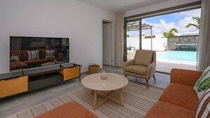 Una sala moderna con televisor de pantalla plana, un sofá, un sillón y una mesita redonda.