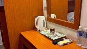Un escritorio de madera con una tetera, un control remoto, una bandeja con un libro y dos botellas de agua.