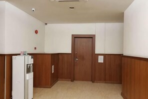 Un pasillo con una puerta de madera, un refrigerador blanco y una cámara de seguridad instalada en la pared.