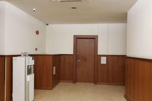 Un pasillo con una puerta de madera, un refrigerador blanco y una cámara de seguridad instalada en la pared.