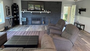 Een woonkamer met een stenen openhaard, een zwarte tv-meubel en een grijze bank.
