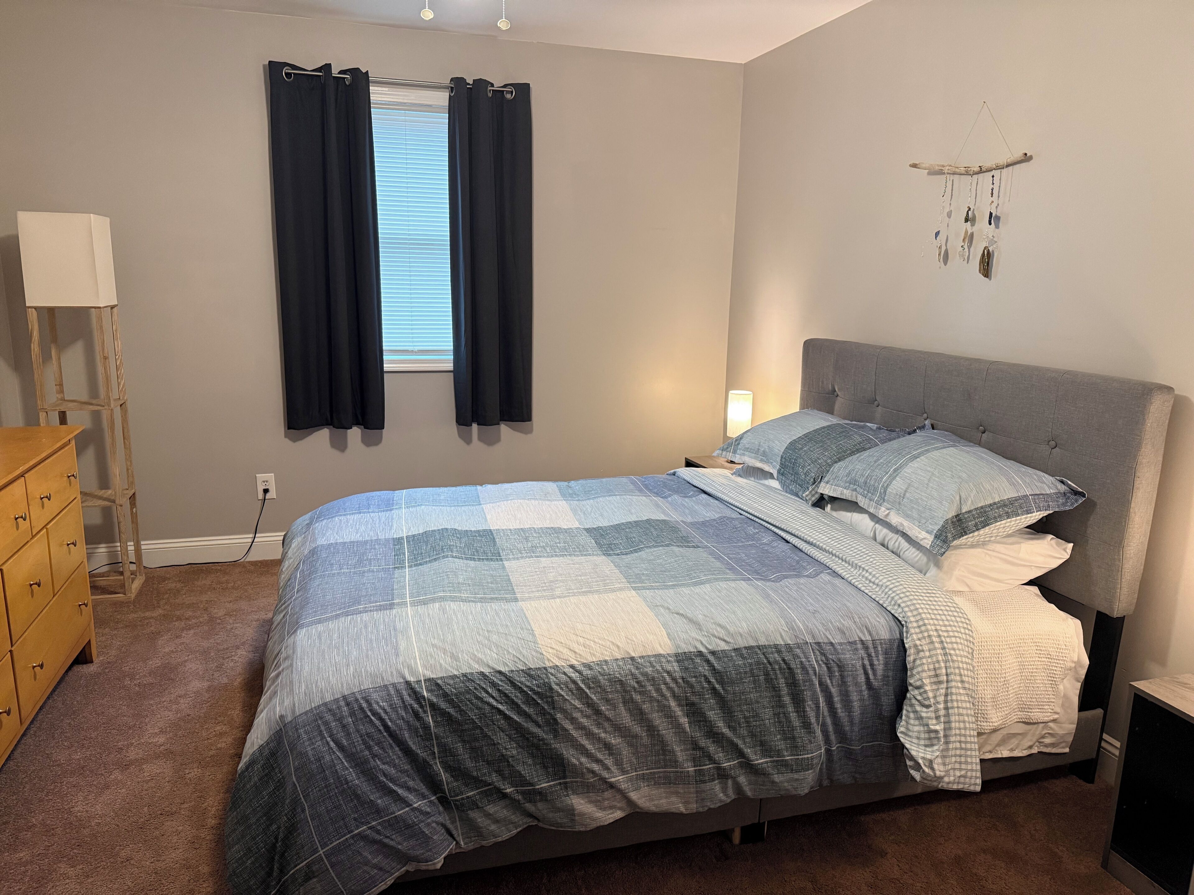 Une chambre à coucher avec un lit, une commode, une lampe et un élément décoratif mural.