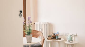 Una habitación pequeña y luminosa con una silla de mimbre, una mesa redonda y un radiador.
