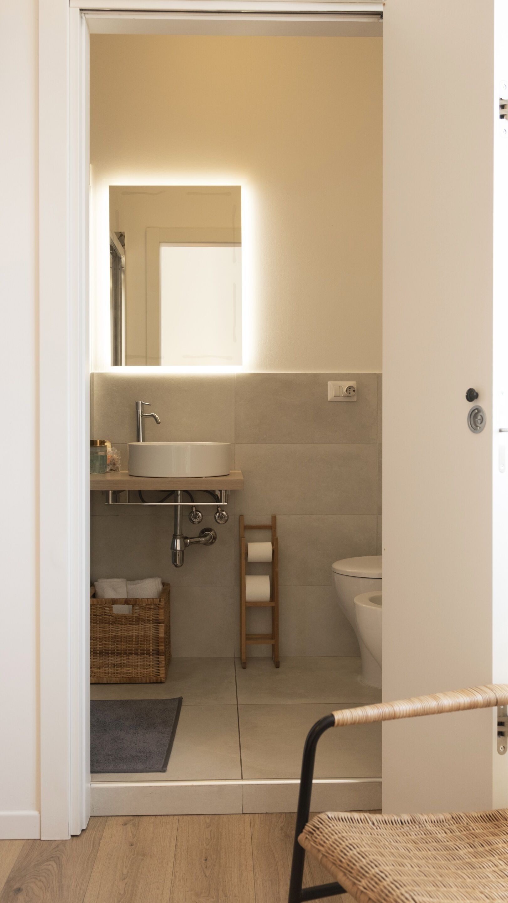 A bathroom with a sink, mirror, toilet, and a small wooden stool.