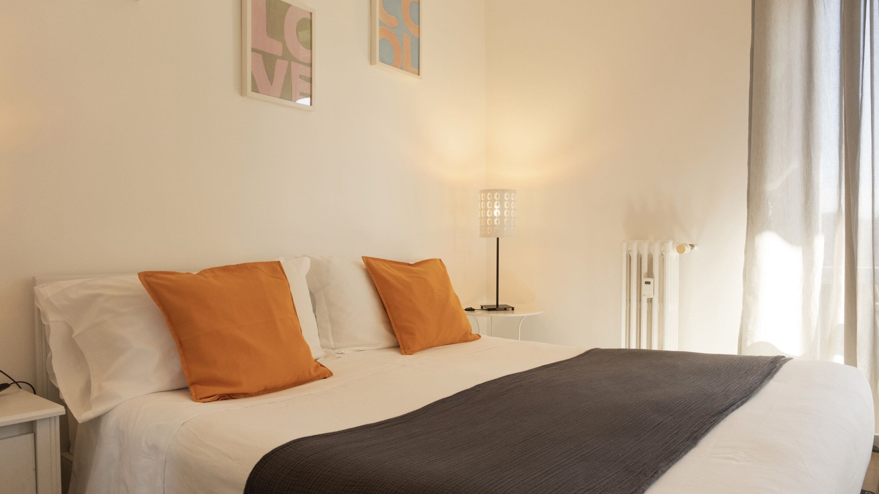 Un letto rifatto con cuscini bianchi e arancioni, una coperta scura e una lampada da comodino.