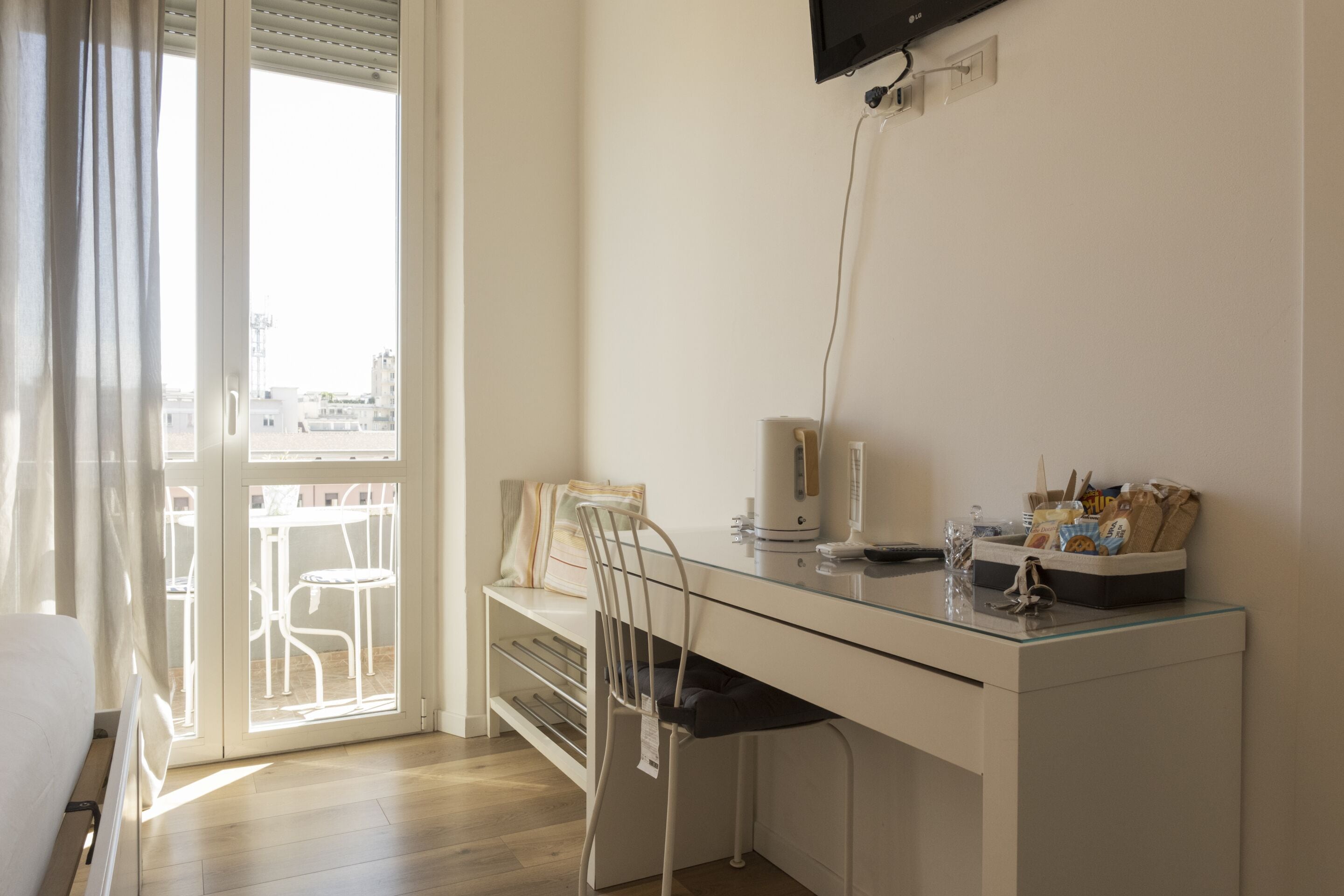 Een moderne kamer met een glazen bureau, een stoel, een bed en uitzicht door een groot raam.