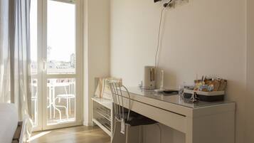 Een moderne kamer met een glazen bureau, een stoel, een bed en uitzicht door een groot raam.