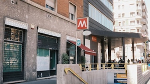 A multi-story building with a prominent 'M' sign, a covered entrance, and a staircase leading to an upper level. - MILANO 71 (Milan)