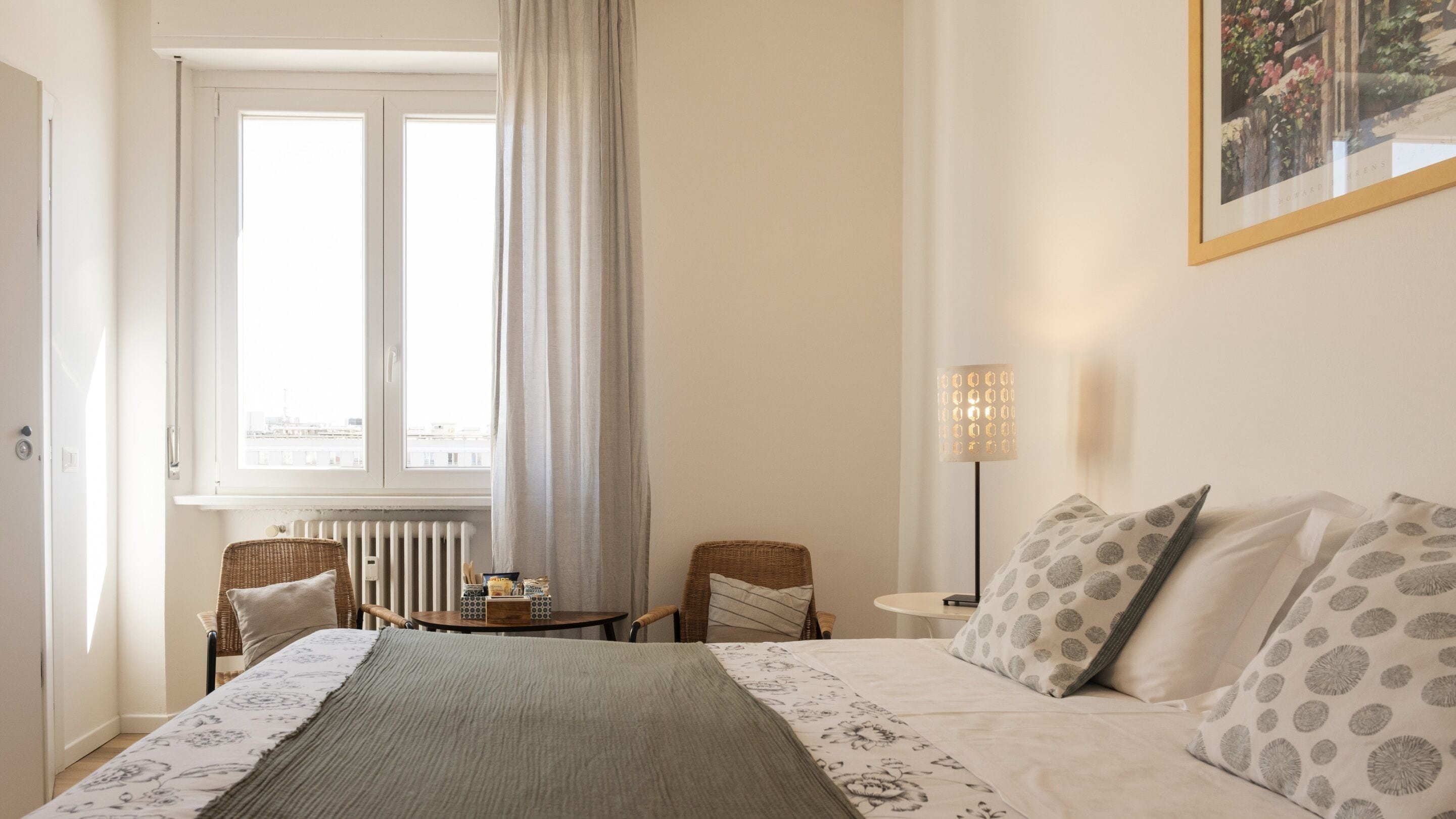 A hotel room with a bed, two chairs, a table, a lamp, and a window with curtains.