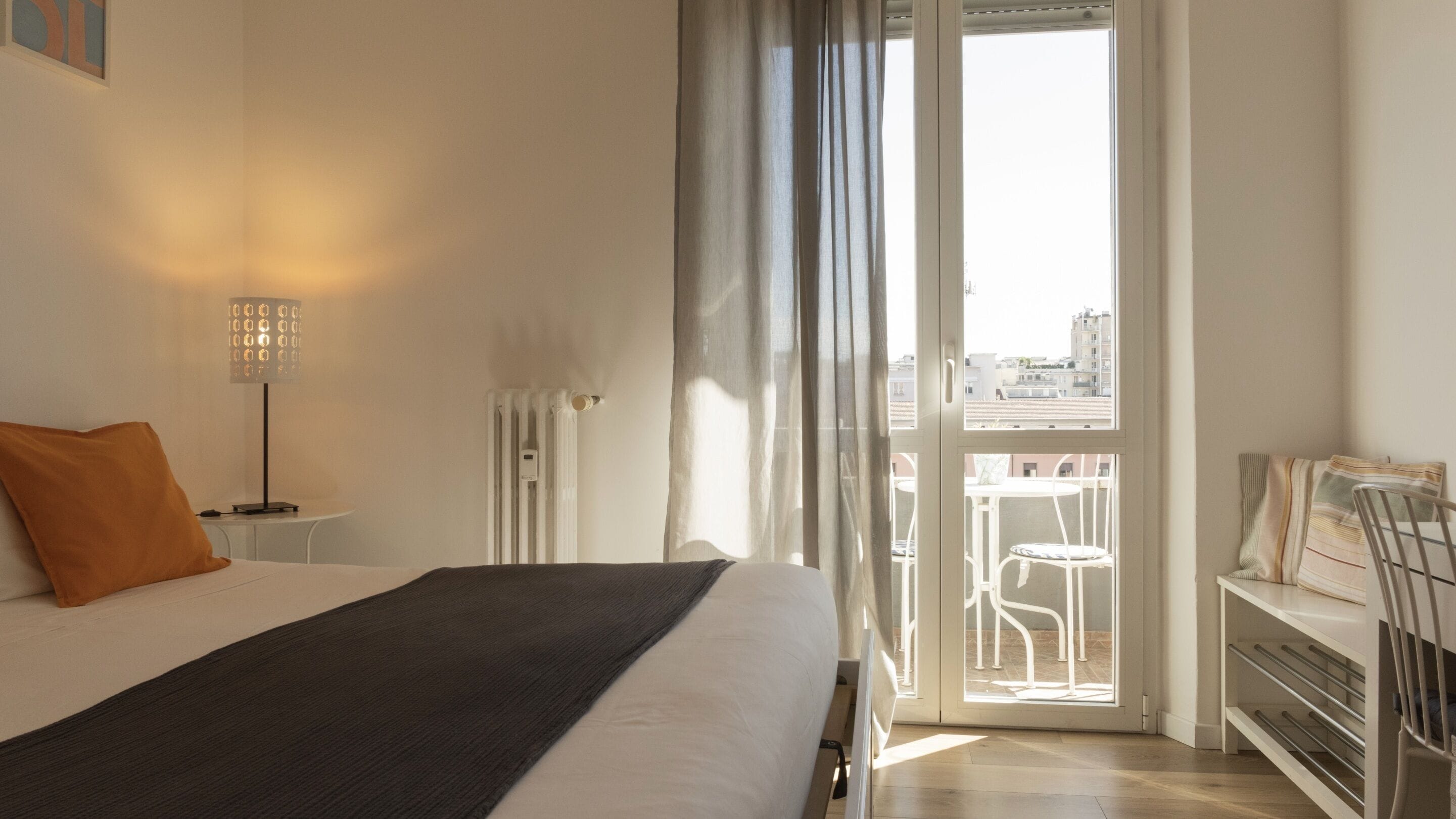 Ein Hotelzimmer mit Bett, Schreibtisch, Stuhl und einem Balkon mit Blick auf Gebäude.