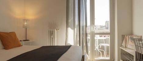 Ein Hotelzimmer mit Bett, Schreibtisch, Stuhl und einem Balkon mit Blick auf Gebäude.