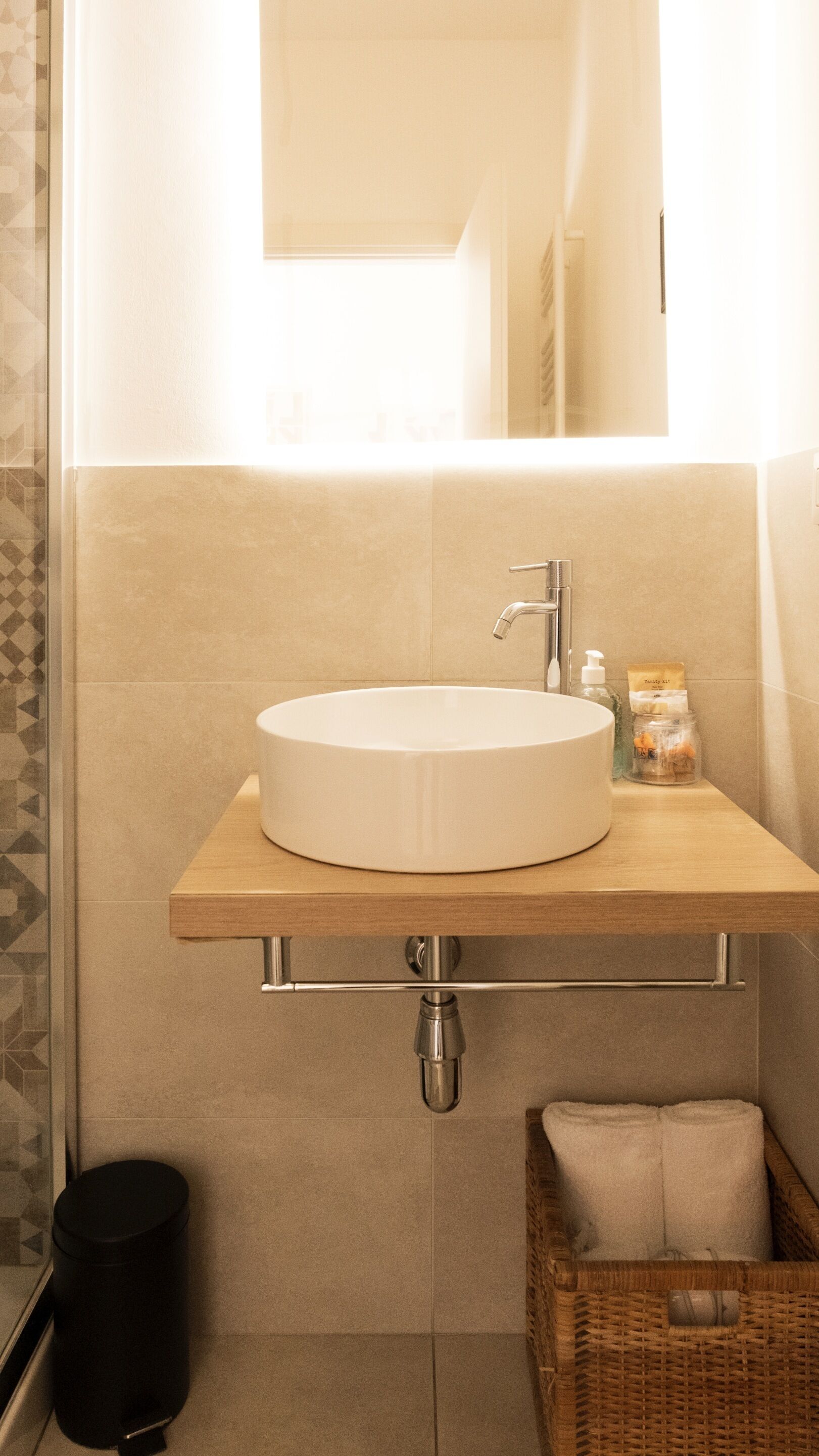 A bathroom with a round sink, a mirror above it, and a small wicker basket with a towel.