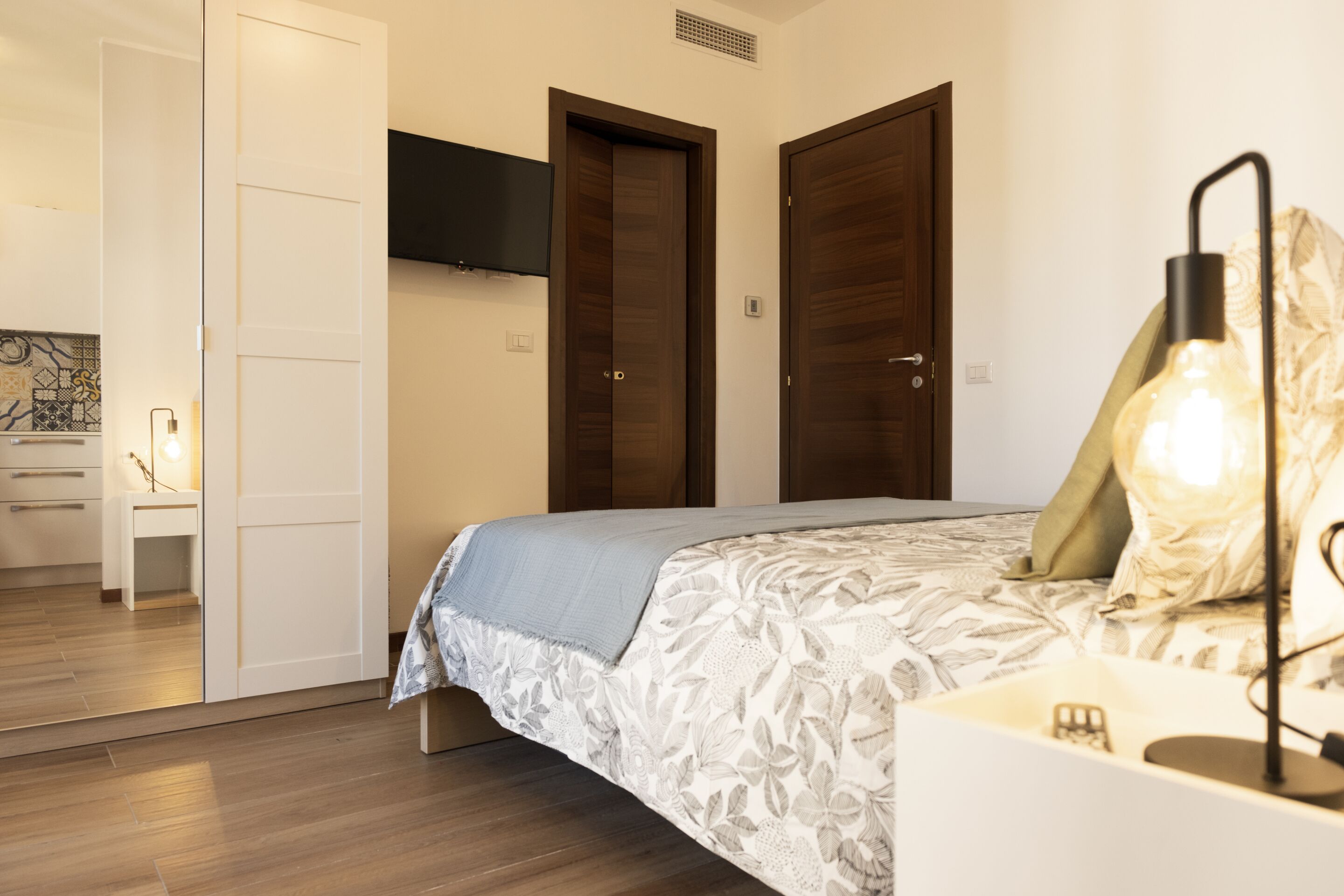 A bedroom with a bed, a bedside table, a lamp, and a wardrobe.
