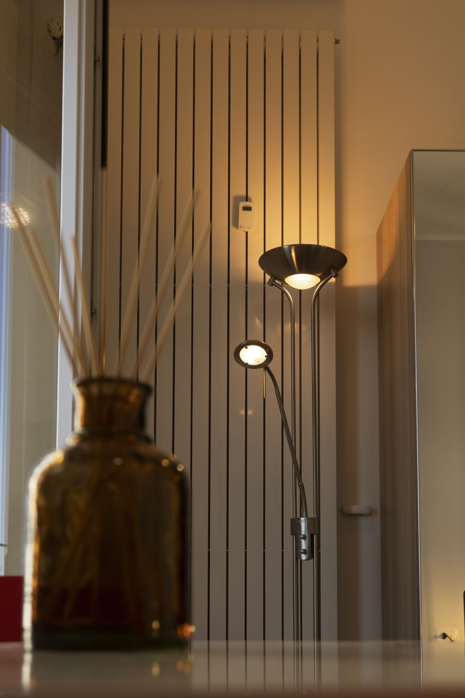 Un interno moderno con una lampada da terra alta e slanciata e un vaso decorativo su un tavolo.