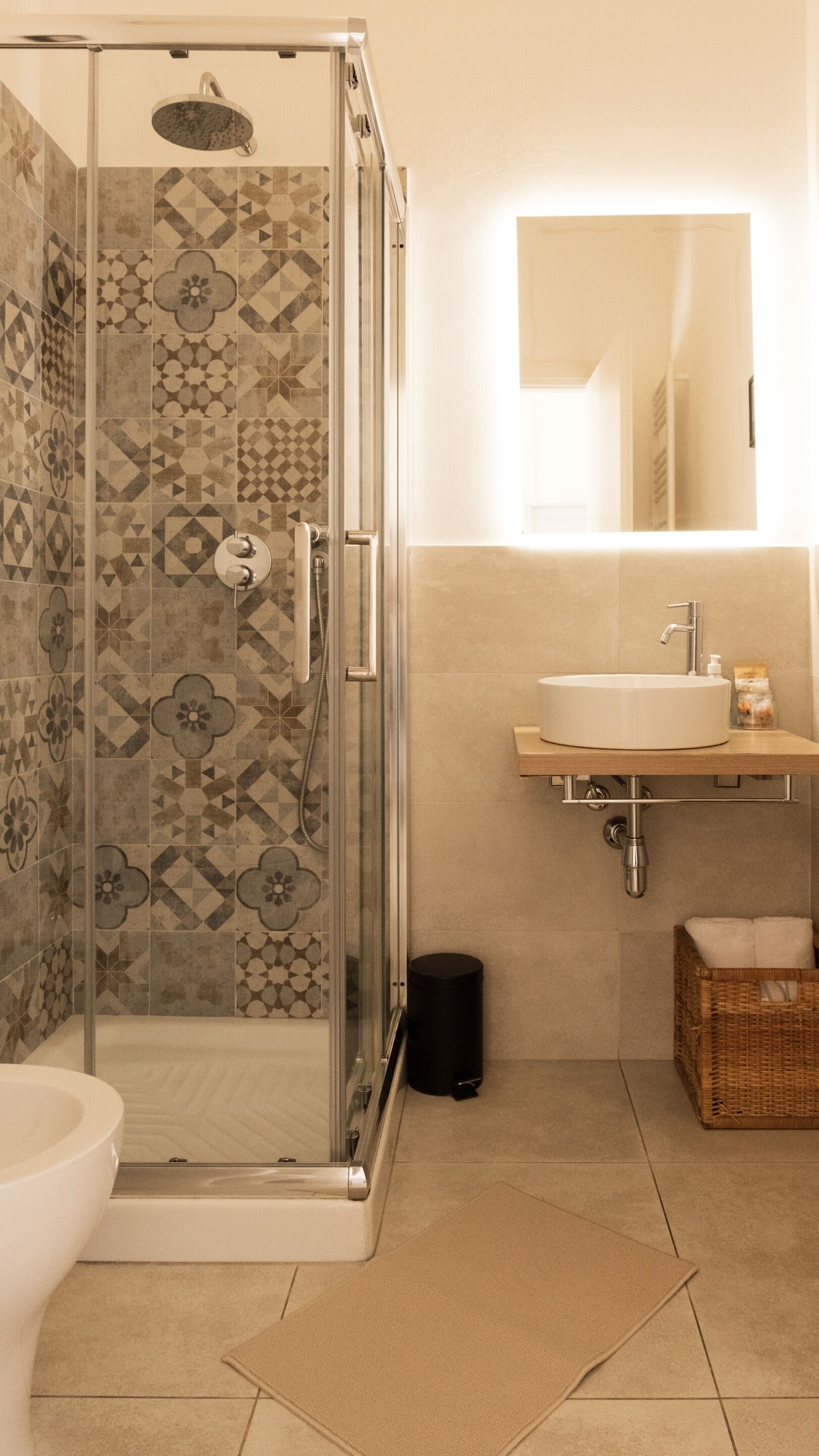 Une salle de bain avec une douche en verre, des toilettes, un lavabo avec un miroir au-dessus et un panier en osier.
