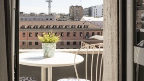 Un balcón con una mesa, sillas, una planta en maceta y vistas a edificios y una torre de comunicaciones.
