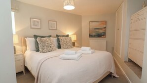 A neatly arranged bedroom with a bed, two bedside lamps, a radiator, and a wardrobe. - Round Barn (Ilfracombe)