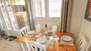 A dining area with a wooden table set for four, white chairs, and a chandelier. - Orby Cottage (Skegness)