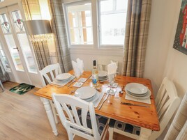 Comedor con mesa de madera dispuesta para cuatro personas, sillas blancas y una lámpara de araña.