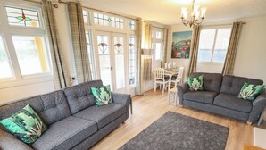 A living room with two grey sofas, a dining table with chairs, and a chandelier. - Orby Cottage (Skegness)