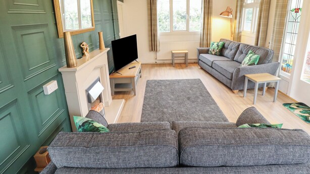 A living room with a sofa, a television, a fireplace, and a window with curtains. - Orby Cottage (Skegness)
