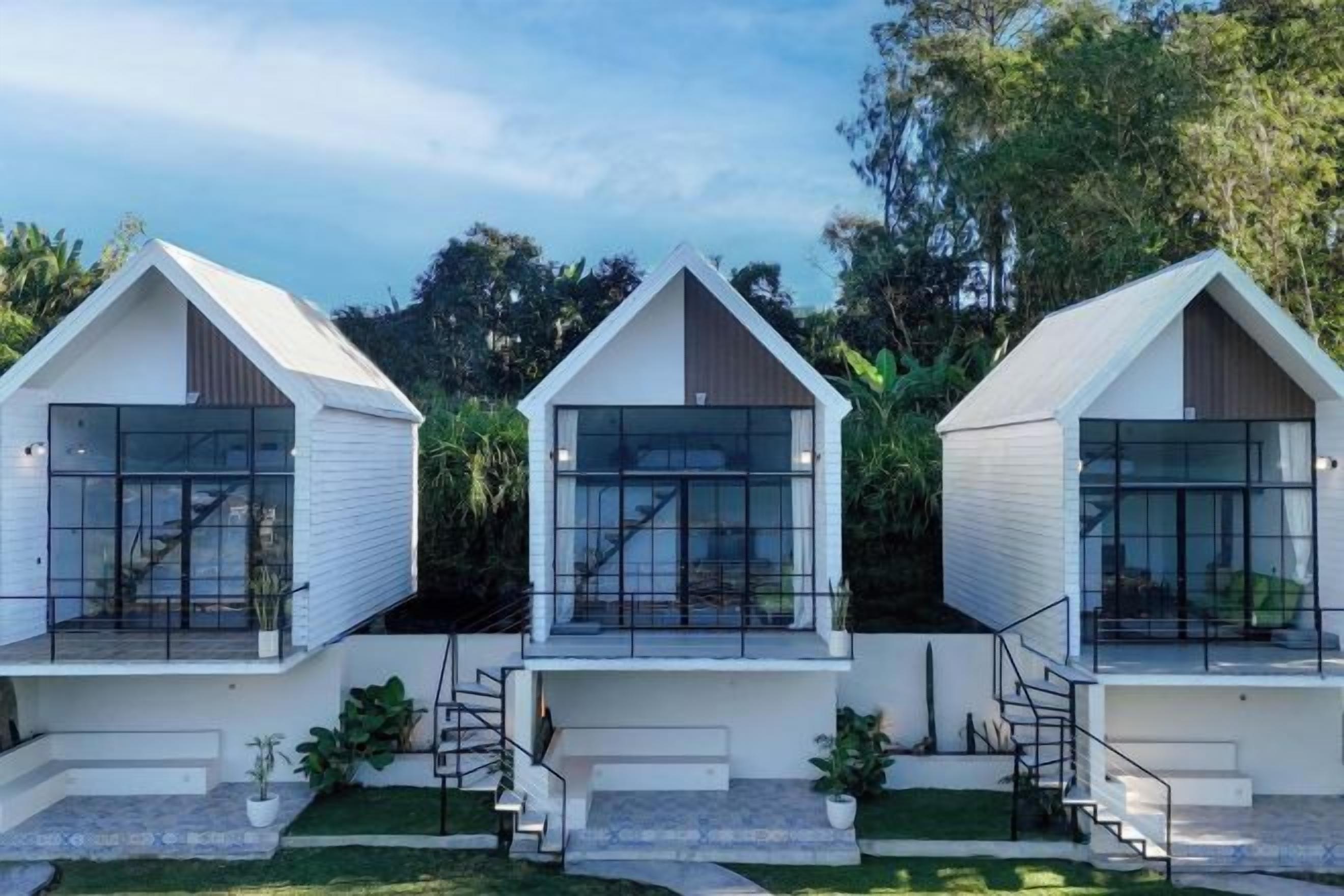Tres estructuras modernas, blancas y con frentes de vidrio, con escaleras externas, ubicadas en un entorno verde y exuberante.