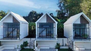 Tres estructuras modernas, blancas y con frentes de vidrio, con escaleras externas, ubicadas en un entorno verde y exuberante.