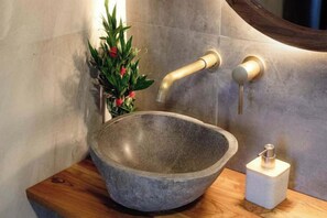 A stone basin sink with a wooden countertop, a wall-mounted faucet, and a small potted plant. - Faro Cabin Kintamani (Bali)